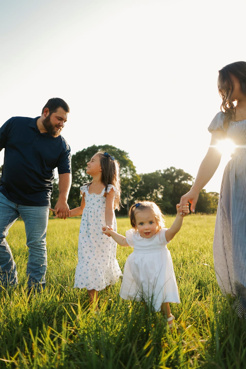 A family of four walking hand in hand through a summer field at golden hour
